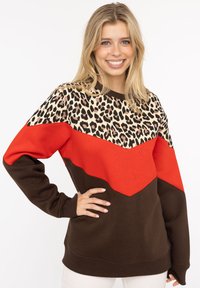 Bluza w kolorowe bloki z górną częścią w leopardzi wzór, dolnymi odcinkami w czerwonym i ciemnobrązowym kolorze oraz ściągaczami przy mankietach i dolnym brzegu.
