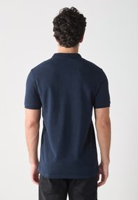 Camisa polo azul marino con mangas cortas, tejido texturizado y cuello plano, con un dobladillo recto y sin logotipos ni patrones visibles.