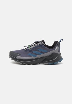 Chaussure de randonnée bleu et gris avec une tige texturée, étiquette GORE-TEX, design élégant et semelle robuste dotée de crampons proéminents pour une meilleure adhérence.