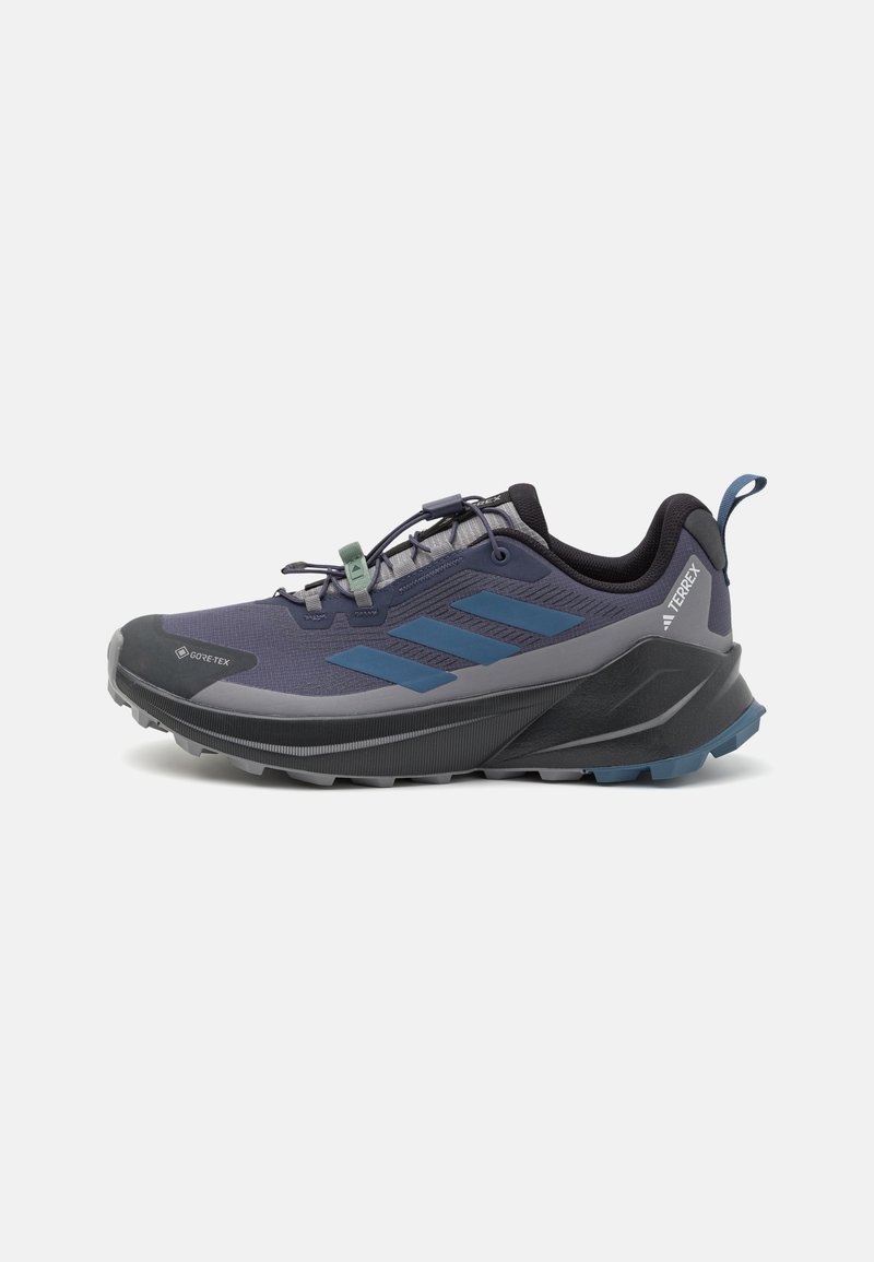Scarpa da trail blu e grigia con tomaia texturizzata, etichetta GORE-TEX, design elegante e suola robusta con prominenti battistrada per una migliore aderenza.