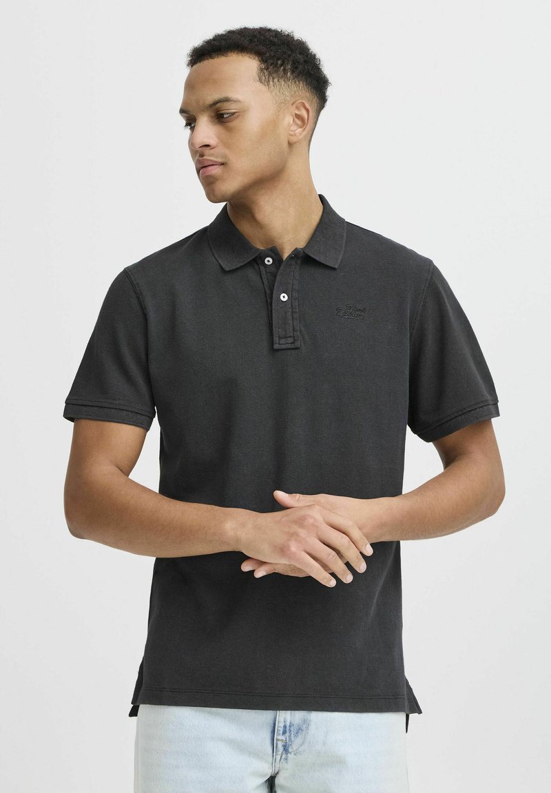 Svart polo-skjorte med korte ermene, tre-knaps placket og brodert logo. Laget av teksturert stoff, med sidespalter for komfort.
