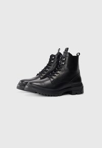 Botas de tobillo de cuero negro con punta redonda, cordones en la parte delantera y suelas robustas. Presentan pequeños ojales de metal y tiradores. Textura suave.