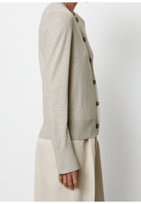 Beżowy kardigan z okrągłym dekoltem, długimi rękawami i zapinany na guziki. Miękka dzianina o fakturze z prążkowanymi mankietami i krawędzią, z subtelnymi poziomymi liniami.