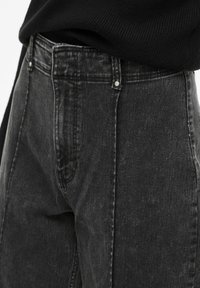 Vaqueros negros de cintura alta en denim desgastado, con corte de pierna recta, costuras visibles y herrajes plateados en la cintura.