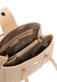 Lysebeige håndtaske med prægede logo-mønster, guldfarvet hardware og en blød stofindvendig med lynlåslomme og åbne rum.