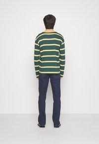 Grön- och gulrandig långärmad skjorta, kombinerad med mörkblå jeans. Skjortan har en rundad halsringning och avslappnad passform.