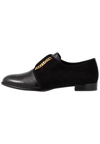 Chaussure en cuir noir et en daim avec une finition lisse, un profil slim et un accent chaîne dorée sur le côté latéral. Talon bas en bloc.