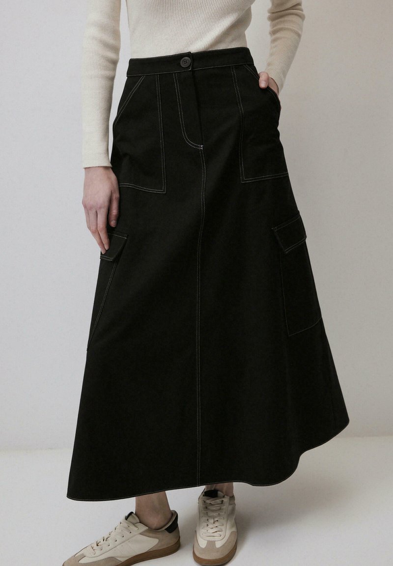 Jupe midi noire avec des détails de couture visibles, deux poches avant et une taille ajustée, associée à des baskets légères. Texture en denim lisse.
