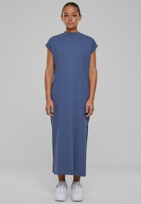 Rochie maxi dintr-un material moale, de culoare albastră închisă, cu mâneci scurte rulate, cu fante laterale și guler înalt, asortată cu adidași albi.