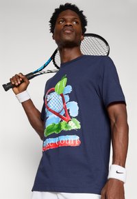 Granatowy bawełniany t-shirt z kolorową grafiką tenisa przedstawiającą rakietę, zielone jabłko oraz napisem "Make Court". Krótkie rękawy, swobodny krój.