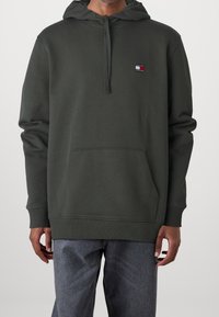Felpa verde scuro con tasca a marsupio, cappuccio con cordino e piccolo logo sul petto. Tessuto morbido, polsini aderenti e vestibilità comoda.