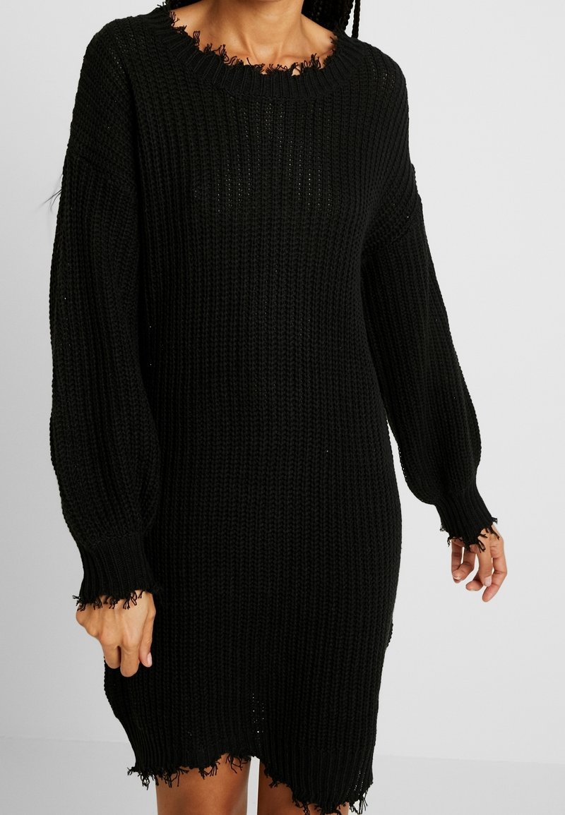 Abito lavorato a maglia nera con una vestibilità ampia, maniche lunghe e bordi sfrangiati. Tessuto testurizzato, collo tondo, lunghezza al ginocchio, caratterizzato da un design a punto aperto.