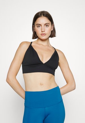 Sutiã desportivo preto com um design em V, apresentando alças finas e um acabamento texturizado, combinado com leggings azuis de cintura alta.