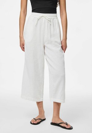 Pantalons blancs à jambe large fabriqués en tissu texturé, dotés d'une taille élastique avec cordon de serrage et de deux poches latérales. Tongs visibles.
