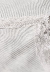Tela blanca con una fina textura acanalada y un borde decorativo de encaje a lo largo de un lado, que presenta intrincados patrones florales y bordes festoneados.