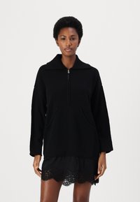 Pullover nero con colletto alto, chiusura con zip e due tasche frontali. Realizzato in materiale morbido, presenta una vestibilità rilassata e spalle scese.