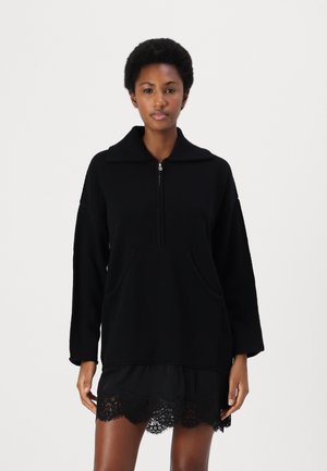Pullover nero con colletto alto, chiusura con zip e due tasche frontali. Realizzato in materiale morbido, presenta una vestibilità rilassata e spalle scese.