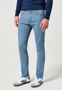 Vaqueros azul claro de corte ajustado, diseño de cinco bolsillos y costuras en contraste, combinados con zapatillas blancas con rayas negras.