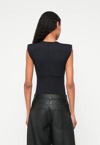 Top preto sem mangas com ombreiras, textura suave, combinado com calças de pele preta de cintura alta com bolsos traseiros e um acabamento mate.