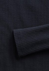 Marineblå ribbestrikket stoff med en teksturert overflate. Bildet viser en nærbilde av en ermedetalj med et mykt, vertikalt mønster.