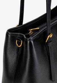 Sac à main en cuir noir avec une texture granuleuse, doté de quincaillerie dorée, de doubles anses supérieures et d'une ouverture zippée.