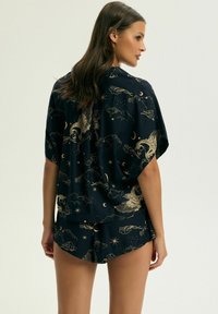 Granatowy komplet piżamowy z złotymi wzorami niebiańskimi i mitycznymi chmurami; luźny krój z krótkimi rękawami i obszytymi szortami. Miękka tekstura tkaniny.