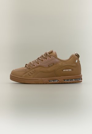 Bruine lage sneaker met veters, gestructureerde zool, luchtkussentje en merklabels aan de zijkant en tong, afgebeeld in zijaanzicht op een neutrale achtergrond.