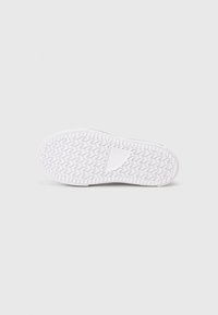 Fehér sneakerszáll rücskös talppal és lekerekített formával. Simaság jellemzi minimális díszítéssel, a tapadás és a tartósság érdekében tervezve.