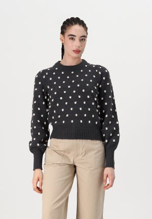 Dunkelgrauer Pullover mit weißen Punkten, runder Halsauschnitt, gerippte Bündchen und Saum, aus strukturiertem Stoff, getragen mit beigen Hosen.