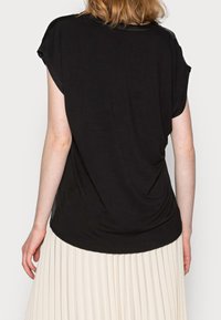 Svart kortärmad topp med avslappnad passform, rundad nederkant och mjuk textur, bärs över en plisserad krämfärgad kjol.