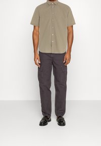 Kortärmad skjorta med knappar i beige, som är kombinerad med mörkgrå cargobyxor med flera fickor och svarta loafers. Slät textur totalt sett.