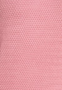 Texturerad tyg i ljusrosa med ett vävt mönster. Materialet har en mjuk känsla och har små, upphöjda noder över hela ytan.