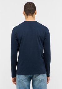 Marinblus med lång ärm i bomull, med rund halsringning och en slät textur, i kombination med ljusblåjeans.