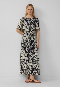 Blumenkleid in Creme und Marineblau, mit kurzen Ärmeln, tailliertem Schnitt und fließender Silhouette. Getragen mit schwarzen Ballerinas.