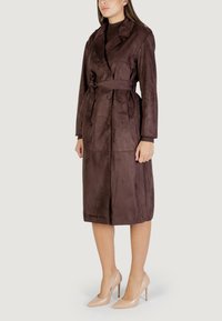 Bruin faux suede trenchcoat met een wikkeldesign, dubbele knopen, lange mouwen en een bijpassende riem, gecombineerd met nude hoge hakken.