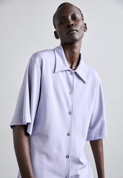 Light purple button-up shirt made of smooth fabric, featuring a pointed collar, short sleeves, and subtle button details.