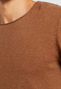 Pull en maille marron avec un col rond, texture côtelée et couleur uniforme, mettant en avant une apparence douce et chaleureuse.