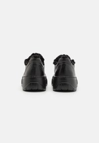 Sorte sneakers med teksturert overdelen, luksuriøse faux fur-detaljer rundt kragen, tykk såle og flate lisser. Minimalistisk design uten synlig merking.