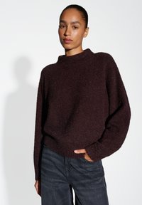 Pull bordeaux surdimensionné avec un col montant, fabriqué en tissu texturé flou, doté de manches longues et de poignets côtelés, porté avec un jean foncé.