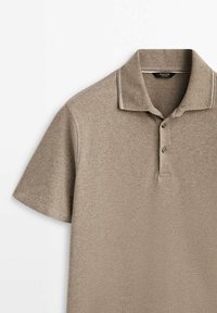 Polo à manches courtes, de couleur brun clair, fabriqué en tissu texturé, avec un col côtelé, deux boutons et des coutures contrastantes discrètes.