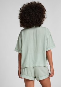 Lichtgroen gestreept overhemd met korte mouwen en bijpassende short. De stof heeft een soepele textuur, met omgeslagen mouwen en een relaxte pasvorm.