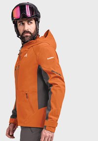 Bright orange ski jacket with gray accents, front zip, multiple pockets, and adjustable hood. Glossy black helmet with tinted visor.