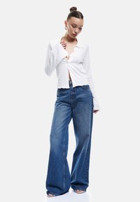 Weiße, strukturierte Bluse mit langen Ärmeln und Kragen, kombiniert mit hochgeschnittenen, weitem blauen Jeans.