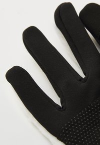 Gant en tissu noir avec de petits points de caoutchouc antidérapants sur la paume, posé sur une surface blanche.