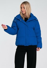 Royal blue puchowy kurtka z wyprofilowanym kołnierzem, zatrzaskami i kieszeniami bocznymi. Wyposażona w pikowany wzór i szerokie rękawy.