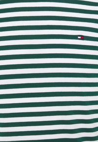 Tessuto a strisce verdi e bianche con strisce orizzontali, texture liscia e un piccolo logo brandizzato nell'angolo in alto a sinistra.