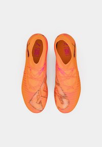 Jasnopomarańczowe buty sportowe z fakturowaną cholewką, ozdobione różowymi akcentami i czarnym logo. Zaprojektowane z eleganckim, aerodynamicznym kształtem.