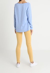 Vaaleansininen pitkähihaisen paita, jossa leveä kaula-aukko, yhdistetty kapeisiin keltaisiin housuihin ja valkoisiin lenkkareihin, rento malli.