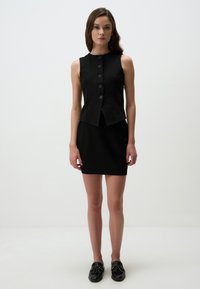 Robe noire sans manches avec un design ajusté, un devant boutonné et un ourlet évasé, associée à des chaussures plates noires.