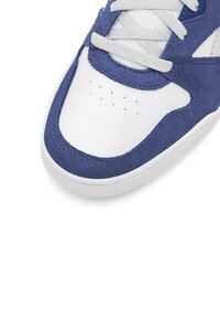 Kék és fehér bőr és velúr felsőrészű sneaker. Kerek orr, lapos talp és szürke fűzők, amelyek szellőzést biztosító perforációkkal rendelkeznek.